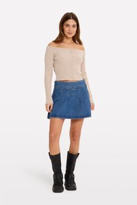 Pulover ușor bej, cu dungi, off-the-shoulder, cu închidere prin buton, asortat cu o fustă din denim albastru închis cu pliuri. Cizme negre, până la genunchi.