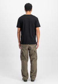 T-shirt en coton noir à manches courtes, porté avec un pantalon cargo vert olive avec poches latérales et coutures décoratives au dos.