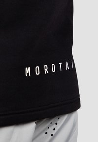 Čierne športové tričko s bielym logom "MOROTAI" na leme. Materiál vyzerá hladko s mierne textúrovaným povrchom.