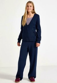 Marineblauwe gebreide wikkeltrui met een v-hals, gecombineerd met bijpassende wijd uitlopende broek. Heeft een ontspannen pasvorm en geribbelde accenten.