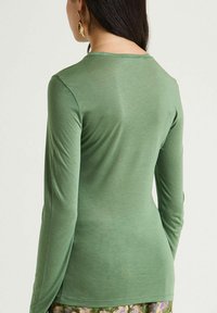 Maglia a maniche lunghe colore verde chiaro, realizzata in materiale morbido. Presenta una scollatura rotonda e una silhouette aderente, con tessuto liscio e senza trama.