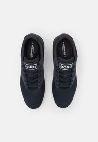 Marina mesh sneakers med svarta detaljer och snörning, med en vit logotyp "BORG" på tungan och en grön cirkulär detalj på insålen.