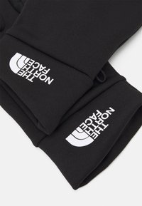 Poignets de sweat-shirt noir en tissu doux, avec un design de texte et de logo blancs. Le texte est en gras et positionné verticalement sur le tissu.