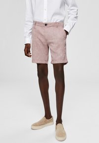 Shorts en lin rose clair avec des ourlets retroussés, poches avant et fermeture à boutons, associés à une chemise blanche à manches longues texturée.