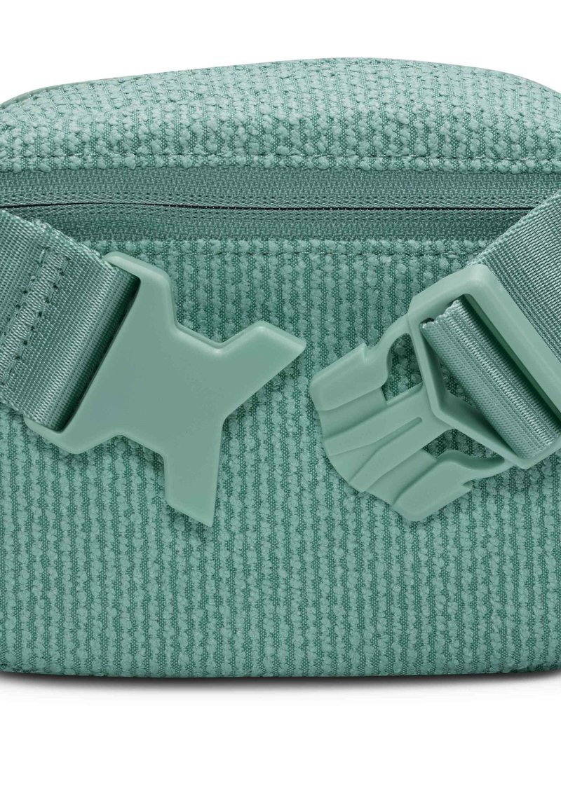 Grüne, strukturierte Tasche mit einem Reißverschluss und kontrastierendem, hellgrünem Plastikbeschlag. Verfügt über einen verstellbaren Gurt und ein einzigartiges, gemustertes Material.