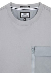 Tricou gri, cu mânecă scurtă și guler rotund, dotat cu un buzunar pe piept cu fermoar și o pană texturată în contrast. Eticheta brandului este vizibilă în interior.