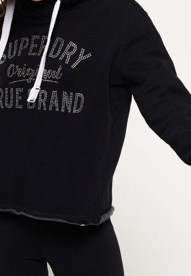 Svart kortärmad hoodie med vita dragsnören. Har metallisk text "SUPERDRY Original True Brand" framtill. Mjuk textur.