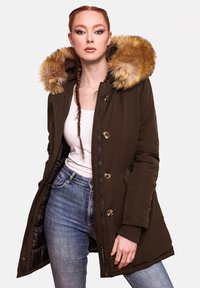 Smeđa parka s kapuljačom obloženom krznom, zlatnim gumbima, dva prednja džepa i zatvaranjem na zip. Nosena preko bijele majice i plavih traperica.