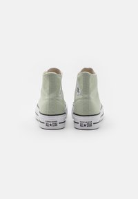 Pár světlých zelených vysokých Converse All Star tenisek pohledem zezadu na jednoduchém bílém pozadí.