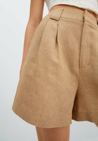 Beżowe spodenki wykonane z fakturowanej tkaniny, z zakładkami, wysokim stanem i bocznymi kieszeniami. Czyste linie i luźny krój.
