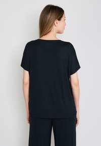 T-shirt noir à manches courtes, coupe décontractée, avec un col rond, fabriqué dans un tissu doux, détails de coutures visibles et ourlet propre.