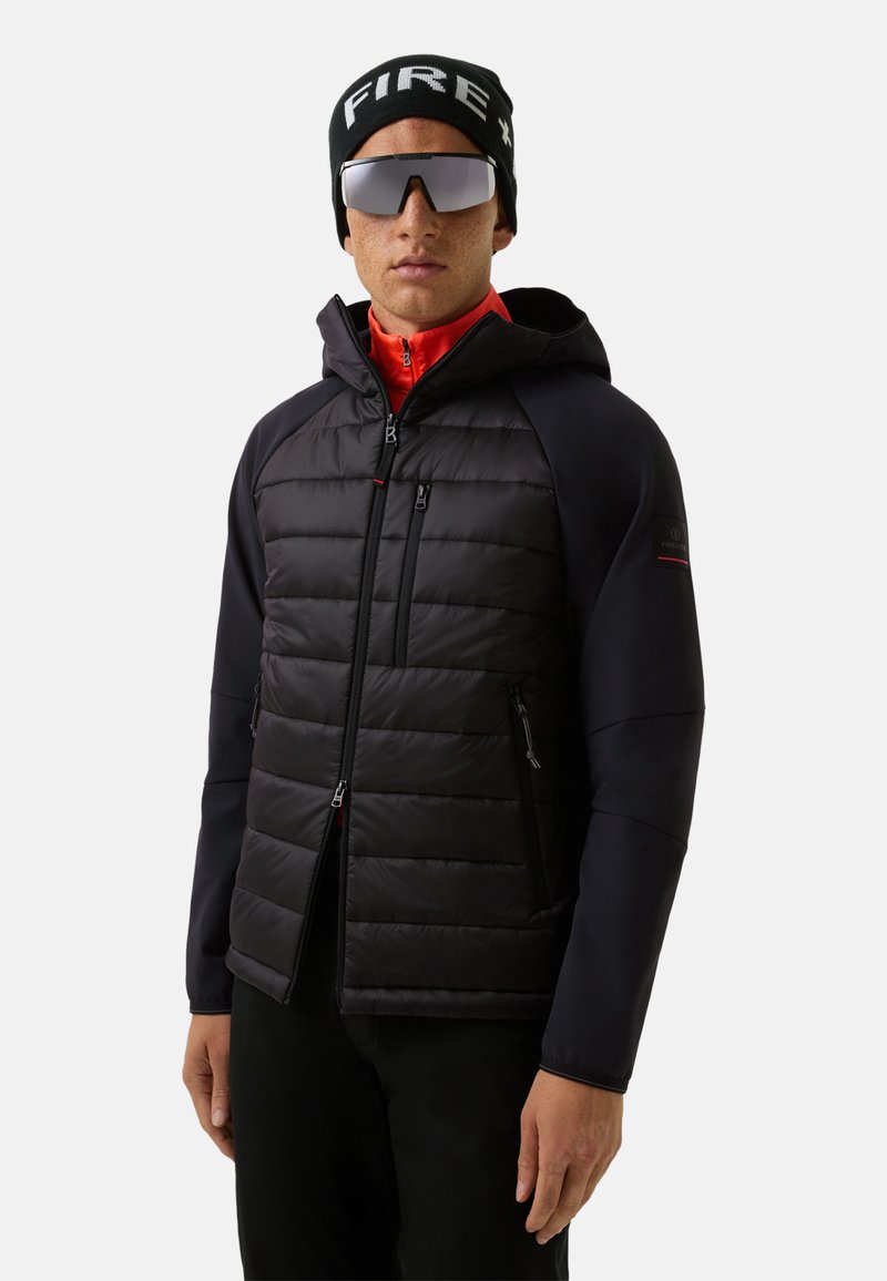 Sort dunjakke med hætte, der har quiltede sektioner og glatte ærmer. Bærendes med et rødt inderlag, sort hue og store solbriller.