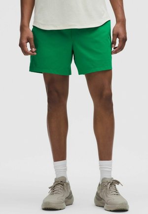 Grüne Shorts aus leichtem Material, mit einem schlichten Schnitt und einem elastischen Bund. Kombiniert mit hellbeigen Sportschuhen und weißen Socken.