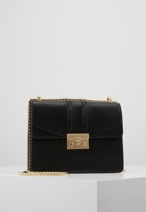 Borsa a tracolla in pelle nera lavorata con chiusura rettangolare dorata e tracolla coordinata in oro, posizionata su una superficie bianca contro uno sfondo grigio.