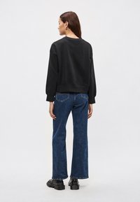 Μαύρο cropped φούτερ με μακριά μανίκια, συνδυασμένο με σκούρο μπλε τζιν παντελόνι φαρδύ στα πόδια και μαύρα πλατφόρμα παπούτσια. Πλάγια όψη της εμφάνισης.