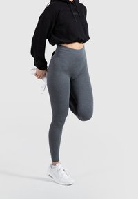 Legginsy o wysokim stanie, prążkowane, w ciemnoszarym kolorze, w zestawieniu z czarną krótką bluzą z kapturem i białymi trampkami z widocznymi sznurowadłami i brandingiem.