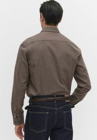 Brun långärmad skjorta med krage, synliga sömdetaljer och knappar, kombinerad med mörk denimjeans och ett flätat bälte.