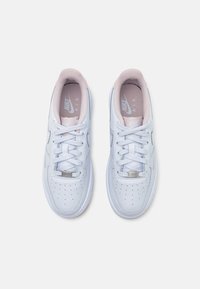 Nike Air kedas baltā ādā ar pastelīgi rozā akcentiem. Iezīmes ietver perforācijas, plakanas baltas auklas un teksturētu iekšējo oderi.