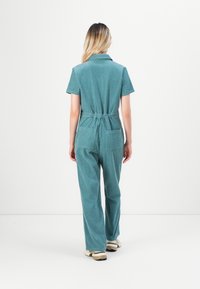 Lys blå jumpsuit med korte ermer, innsvingt midje og to baklommer. Har krage og brede, komfortable benåpninger.