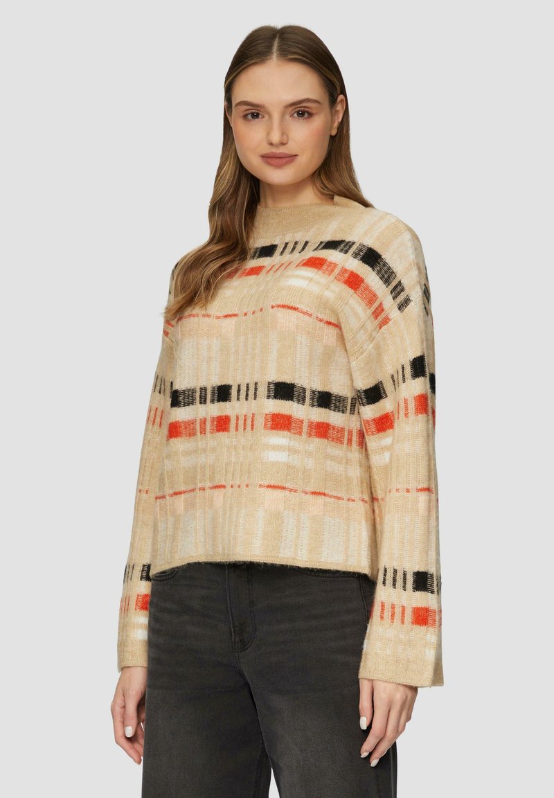 Pull en mailles beige avec des motifs rayés en rouge, noir et crème. Coupe décontractée, col montant et manches larges ; texture douce.