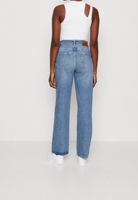 Jeans de tiro alto y pernera amplia en azul claro, con un diseño clásico de cinco bolsillos y una etiqueta de cuero marrón en la parte trasera. Textura de denim suave.