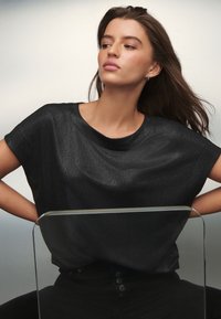 Melnas īsām piedurknēm topiņš, izgatavots no gludas audumu ar vaļīgu piegriezumu, ar apli apkakli un nemanāmu spīdumu, kombinēts ar melnām augstām biksēm.