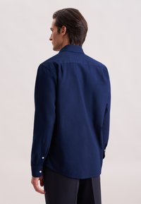 Maglietta a maniche lunghe blu navy con colletto, polsini con bottone e orlo dritto. Realizzata in un tessuto liscio con una texture sottile.