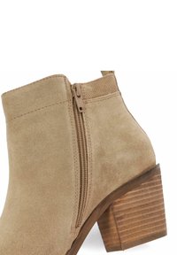 Bottine en suede beige avec une fermeture éclair sur le côté, tige texturée et un talon en bois empilé avec des lignes horizontales.
