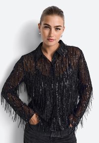 Cămașă neagră cu paiete, având detalii cu franjuri, cu guler și mâneci lungi. Material transparent cu un finisaj texturat.