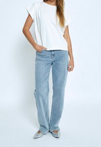 Bílý krátký rukáv top, světle modré džíny s vysokým pasem a stříbrné zdobené baleríny. Oblečení má volný střih a jemné textury látek.