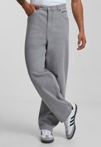 Gray denim pants with a relaxed fit, featuring front pockets, a button closure, and a straight leg design paired with white and black sneakers.