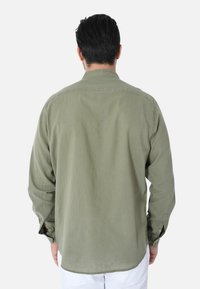 Camicia a maniche lunghe color verde oliva con colletto e polsini a bottoni. Tessuto morbido con una texture liscia, presenta un orlo dritto e senza motivi visibili.