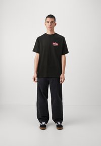 Sort bomulds t-shirt med afslappet pasform, med et rødt og hvidt "ZOOYORK" logo på brystet. Sæt sammen med brede sorte bukser og sneakers.