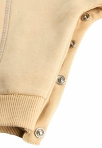 Beiger Strickstoff mit einem gerippten Bündchen und silbernen Druckknöpfen an der Seite, der das strukturierte Design und die Verschlussdetails hervorhebt.