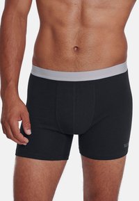 Boxer en coton noir avec une ceinture élastique grise, design ajusté et détails de couture discrets. Uni, sans motifs ni logos.