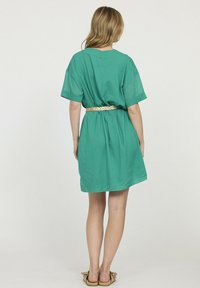 Robe en coton vert à manches courtes, coupe ample, avec une ceinture tissée à la taille. Texture lisse, longueur au-dessus du genou.