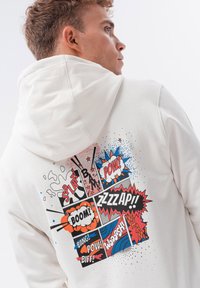Sudadera blanca con gráficos coloridos al estilo de cómic que presentan palabras como "BANG!" y "POW!" en negro y acentos vibrantes de azul, rojo y naranja.