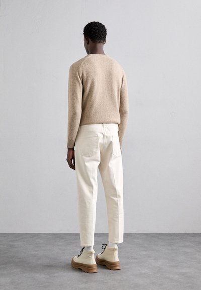 Suéter de punto beige, pantalones crema con corte tapered y botas de tobillo beige con cordones negros. Diseño simple, costuras visibles y tela texturizada.