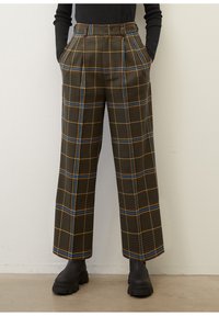 Bruna rutiga byxor med blå och gula ränder, vida ben, hög midja och framfållar. Matchas med svarta kraftiga stövlar.