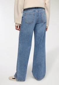 Jeans in denim blu a gamba larga con vita alta, dotati di due tasche posteriori, con una finitura sbiadita e un orlo che arriva sopra le scarpe.