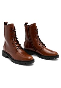 Bottes courtes en cuir marron avec lacets à l'avant et fermeture éclair latérale, semelle en caoutchouc noir texturée et détails de couture.