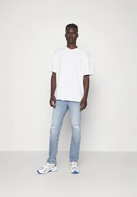 Hvit oversized t-skjorte kombinert med lyseblå slitte jeans og hvite joggesko med blå detaljer. Enkel, avslappet streetwear-design.