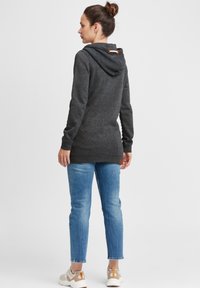 Grå, huva tröja med en strukturerad finish, prydd med en träspänne, parat med ljusblå jeans och neutrala sneakers.