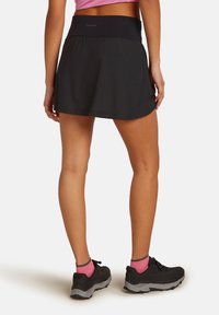 Svart idrotts-skort med bred midjeband och en utsvängd design. Bärs med svarta skor och rosa ankelsockor. Lättviktig, slät textur.