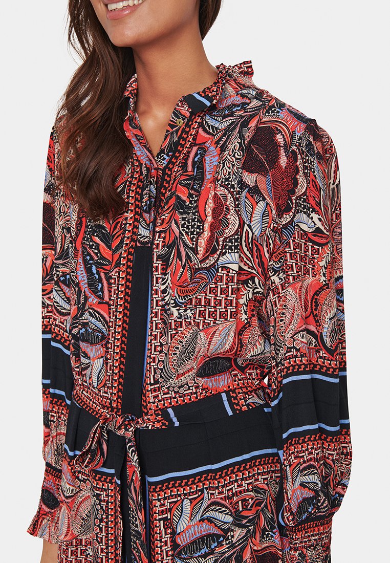 Bluzka w kwiatowy wzór z falbaniastym kołnierzykiem, długimi rękawami i wiązaniem w talii, w odcieniach czerwieni, czerni i niebieskiego, z teksturowanym wykończeniem.
