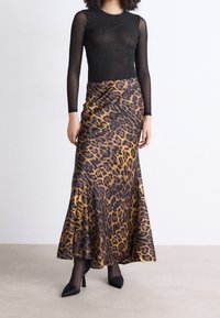 Top de malla negro de manga larga combinado con una falda maxi de estampado de leopardo que presenta un dobladillo acampanado. La falda tiene una textura suave y brillante, y se lleva con tacones negros.
