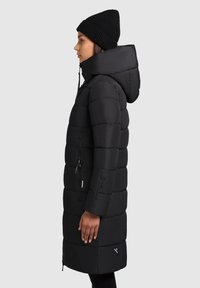 Čierna pufová bunda s kapucňou, s prešívaným dizajnom, so zipsovými vreckami a nastaviteľným šnurovaním. Hladká textúra, dĺžka po kolená.