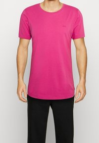 T-shirt a maniche corte con collo rotondo in cotone rosa vivace. Presenta un logo discreto sul petto e un orlo dritto per una vestibilità rilassata.