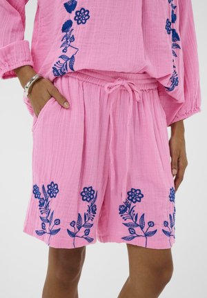 Pantaloni scurți din țesătură roz cu textură, broderie florală albastru închis, talie elastică cu șnur și buzunare laterale, purtați cu un top asortat.