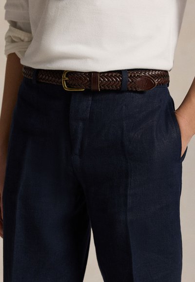 Fonott barna bőr öv aranyszínű csattal, sötétkék, texturált nadrág felett viselve. Laza, kényelmes fazont kínál.
